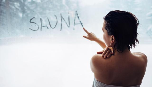 Frau schreibt mit dem Finger das Wort Sauna an eine beschlagene Scheibe